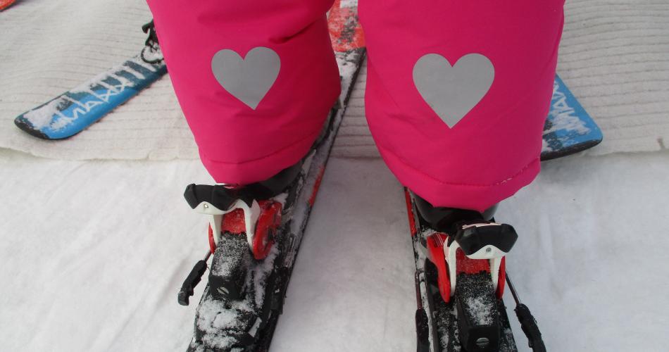 Kinderbeine von hinten in Skibindung und Herzen auf der Hose