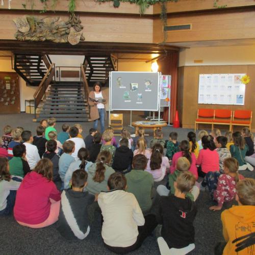 Kinder in der Aula, Lehrerin liest ein Buch vor