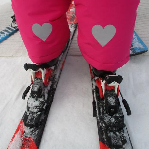 Kinderbeine von hinten in Skibindung und Herzen auf der Hose