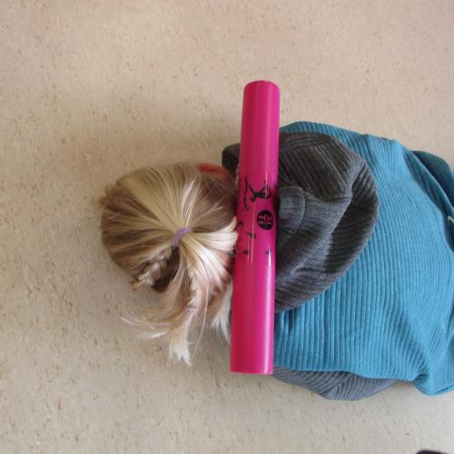 Kind kniet am Boden und hat einen Boomwhacker auf dem Rücken liegen